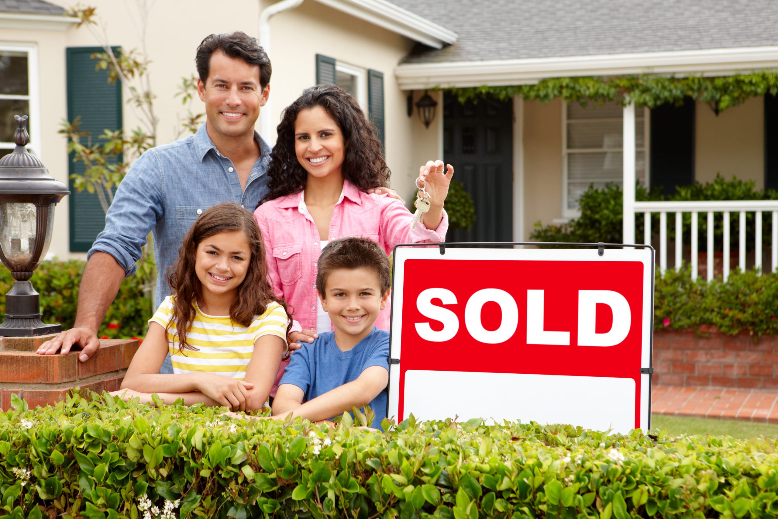 Dad, mom, daughter and son outside home next to red sold sign